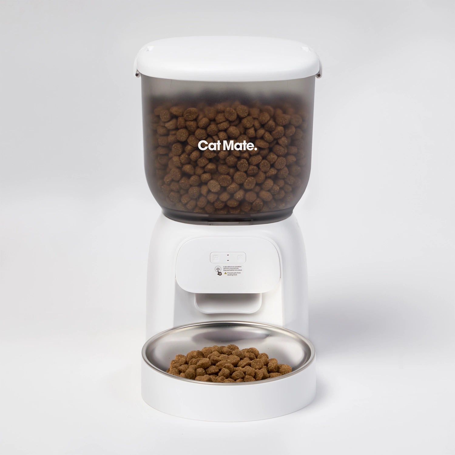 A white Cat Mate automatic pet feeder filled with dry cat food, shown on a clean white studio background. The feeder has a clear upper container, a white dispensing base, and a stainless steel bowl at the bottom.