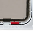 Close-up view of the right hand corner of a white cat door frame with a red manual lock, clear flap and grey draft proof brushing above a 'Lock' label, on a white background
