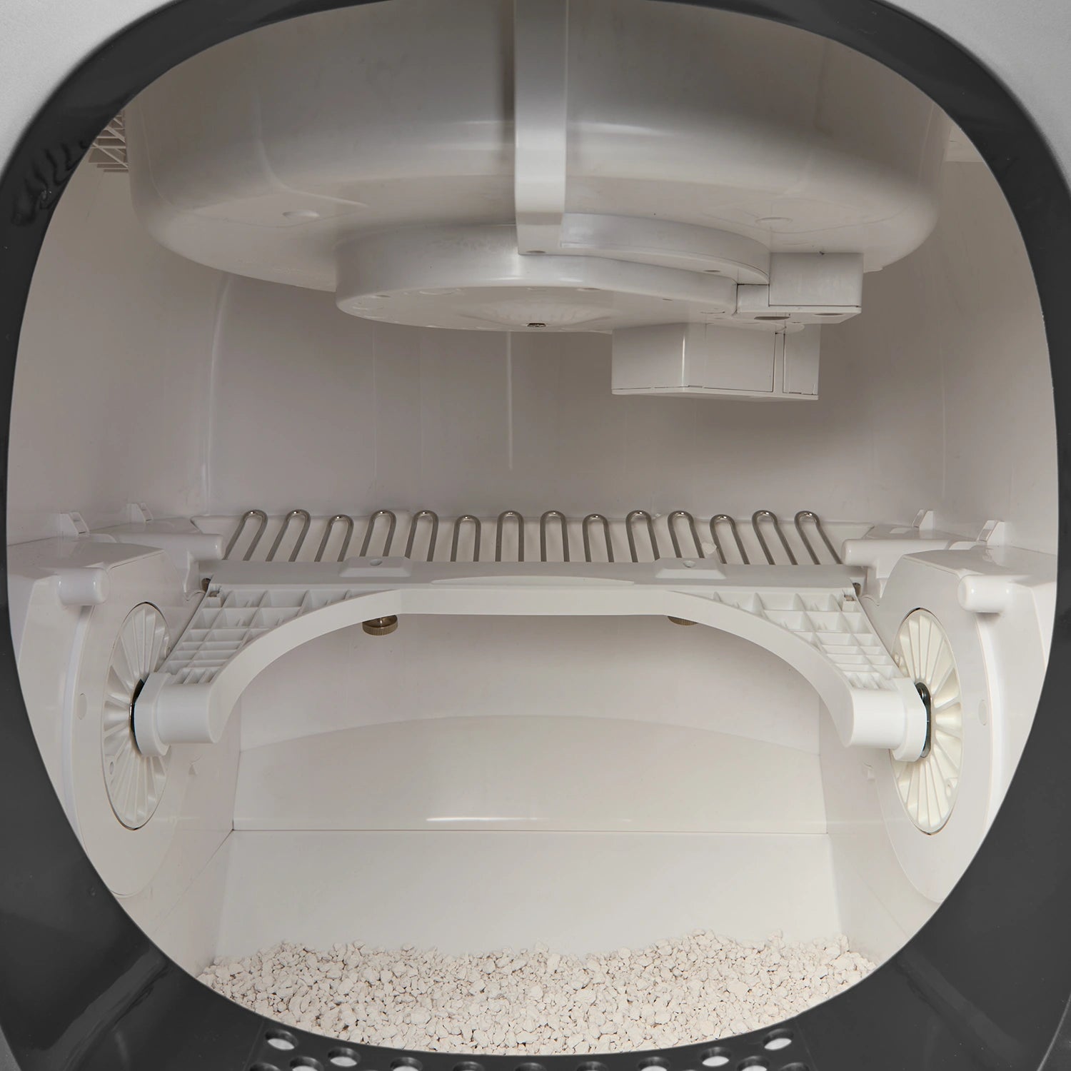Interior view of Cat Mate automatic litter box showing white cleaning rake mechanism with comb-like tines positioned above litter bed, with waste collection area visible at back and smooth curved walls