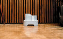 Close-up of a white 'CAT MATE' pet water fountain placed on a polished concrete floor in front of a modern wooden slat wall. Water is visibly flowing from the upper tier to the lower tier of the fountain, highlighting its multi-level design.