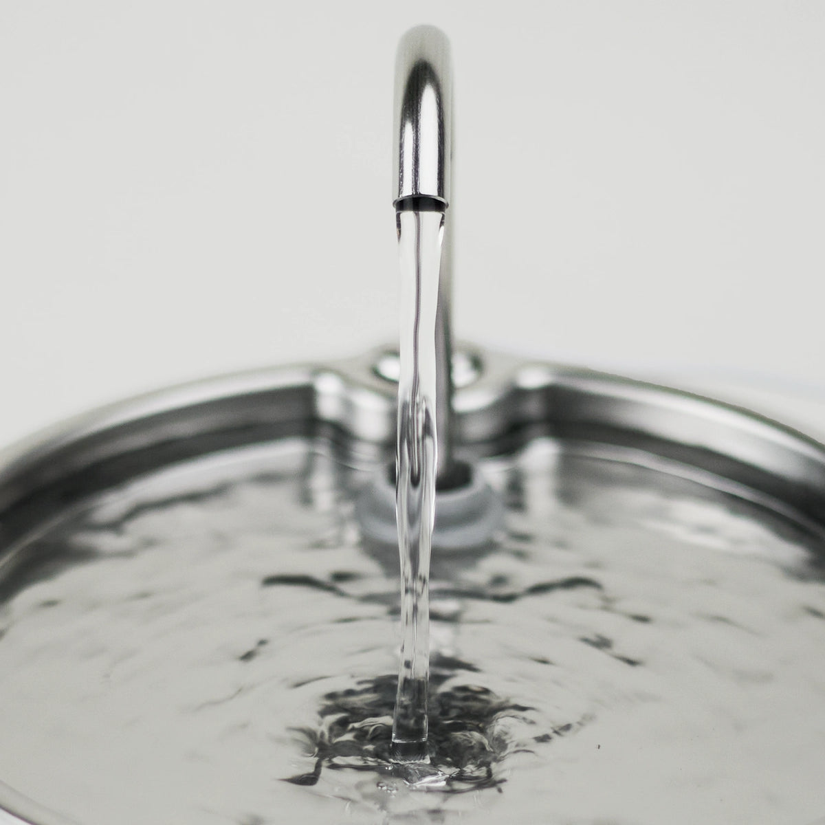 A close-up of the stainless steel faucet spout on the Cat Mate 2.2L stainless steel fountain dispensing a clear stream of water into the water tray shown against a light neutral background.