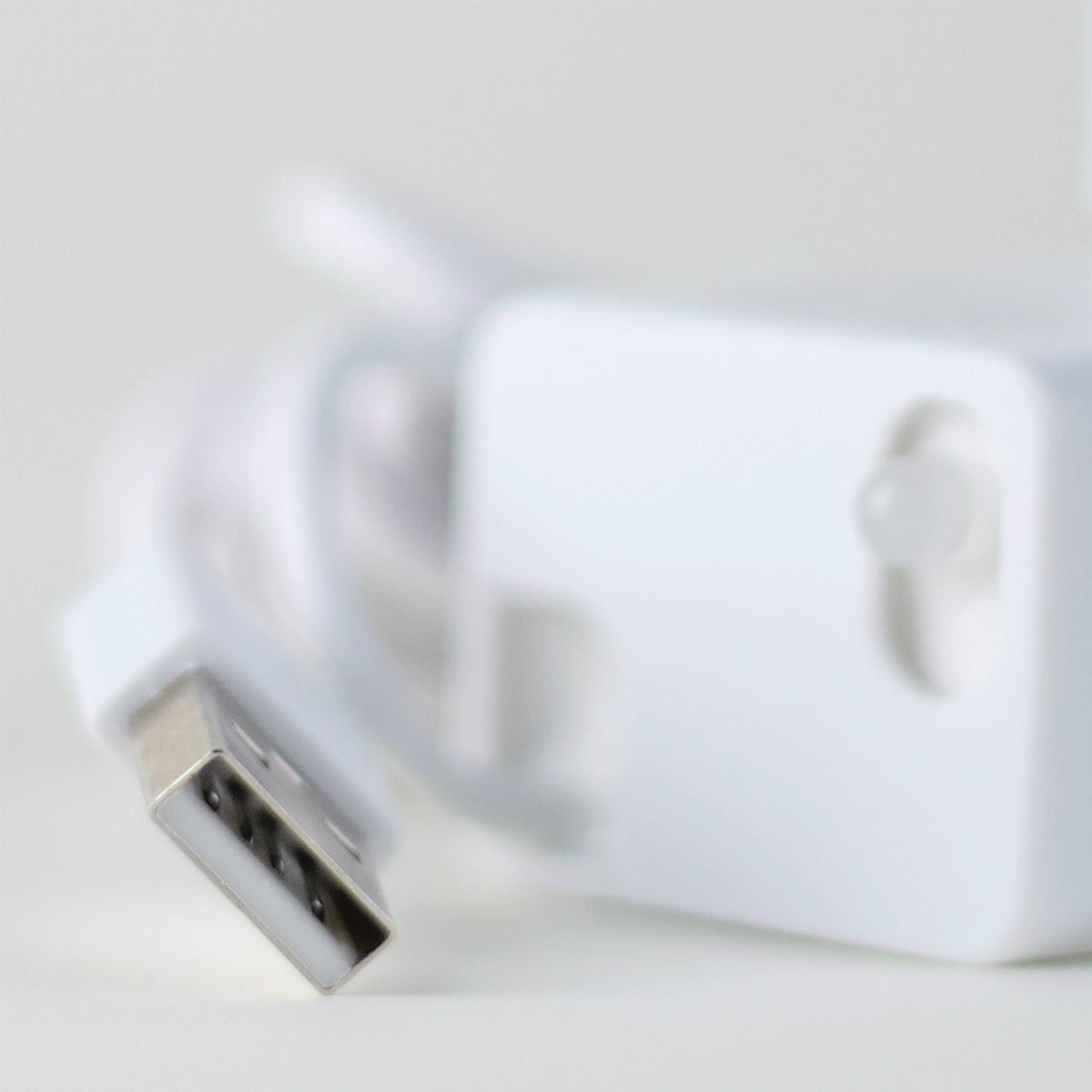 Close-up of the Cat Mate fountain's white USB cord and connector in sharp focus, with the white pump unit blurred in the background.