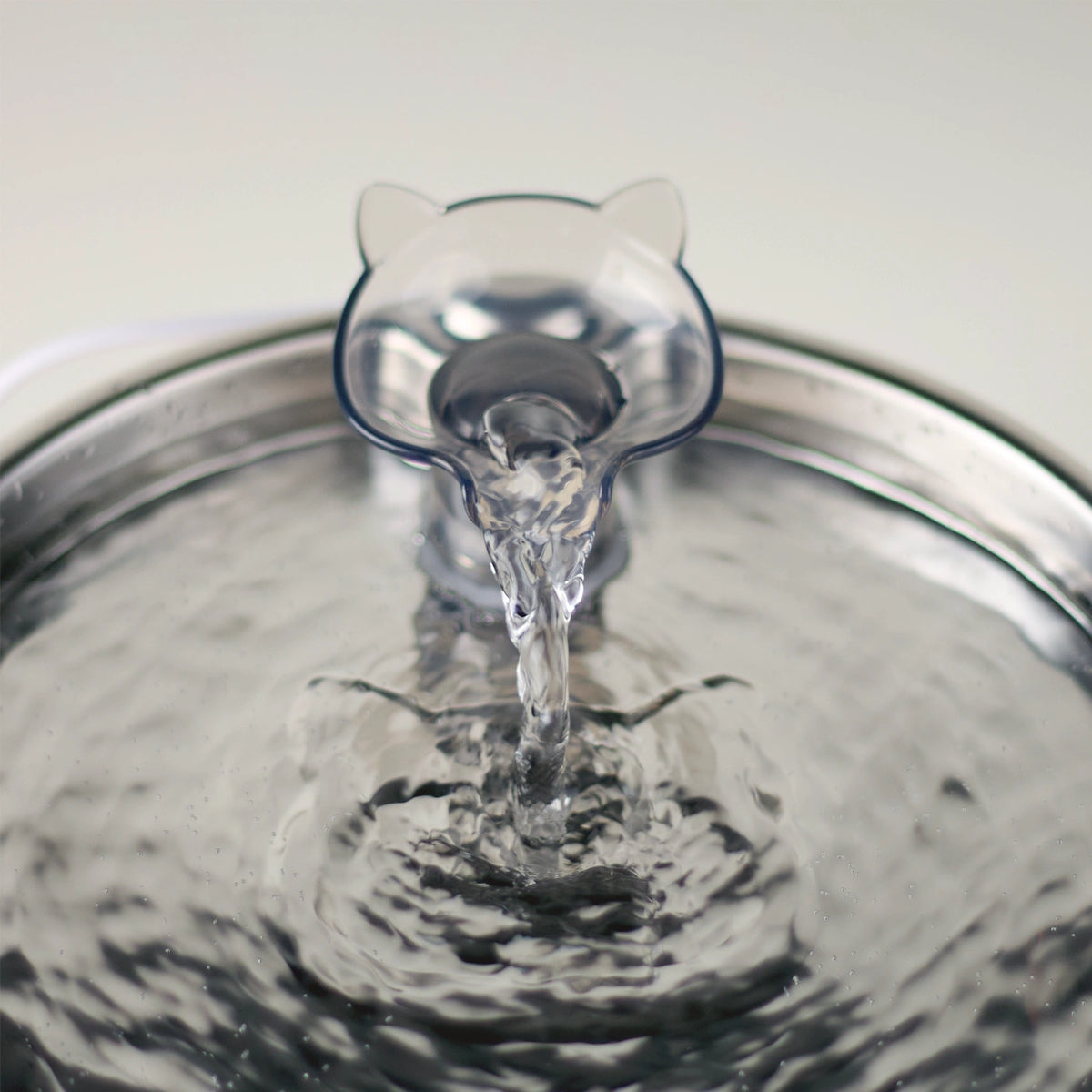 A detailed closeup of the acrylic cat-head-shaped interchangeable faucet spout on the Cat Mate 2.2L stainless steel fountain, with water pouring from the spout into the stainless steel bowl against a white background 