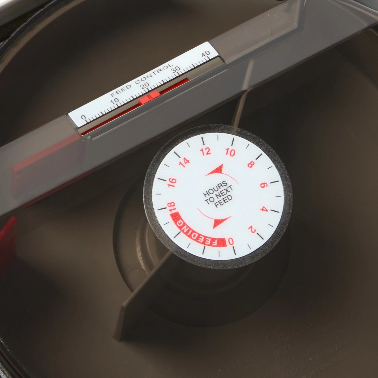 A dark coloured fish feeder specifically designed for use with ponds and pond fish, with an analogue display and food control panel on a dark background