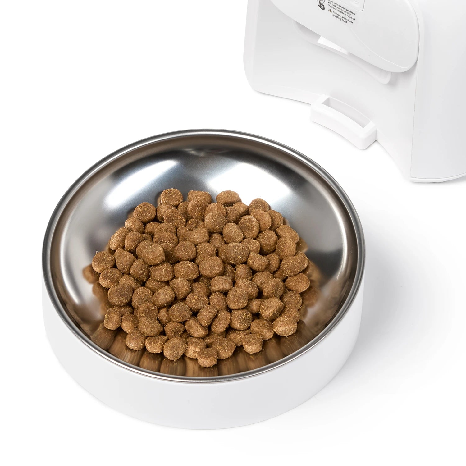 A white pet feeder bowl made by Cat Mate, filled with brown kibble, with part of the white feeder unit visible in the background on a clean white surface.